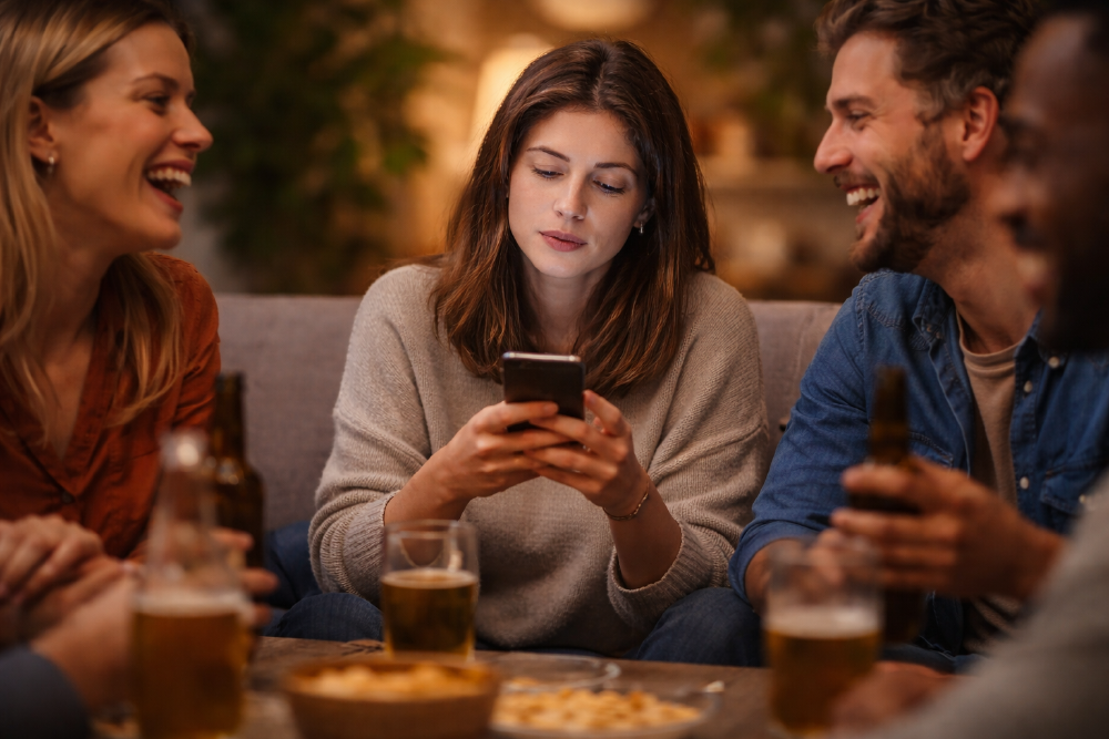 A woman looking at her phone while the friends around her laugh together